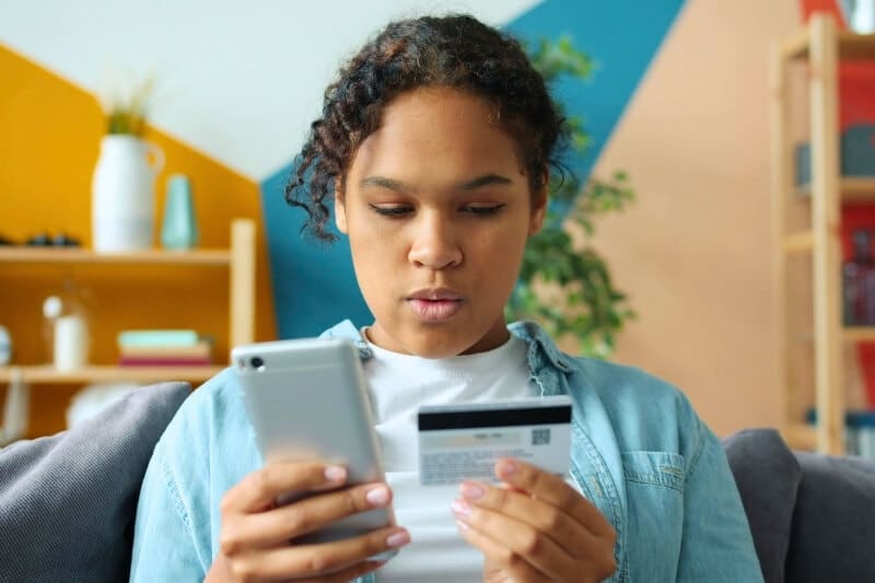 Young woman on a sofa looking at her smartphone while holding a credit card