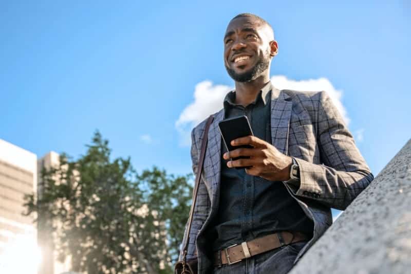 Smiling man in a checked blazer holding his phone, looking up at a blue sky