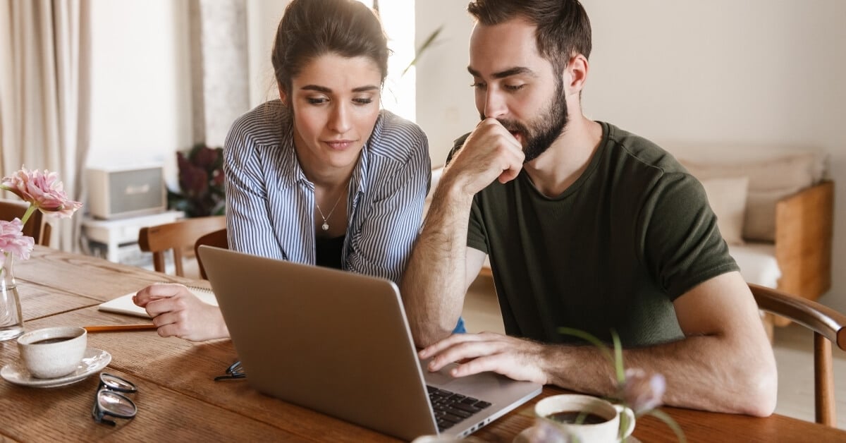 Two people seated at a table reviewing something on a laptop together